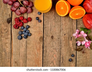 Orange Juice, Fresh Oranges, Apples, Grapes, Raspberries, Blueberries And Spring Flowers On A Wooden Table - View From Above