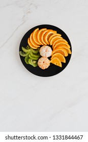 Orange And Kiwi On Black Plate. White Marbel Background. Food Styling With Copy Space  