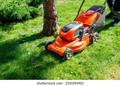 Orange Lawn Mower On Wheels On Green Fresh Grass. Grass Mowing Process, Top View