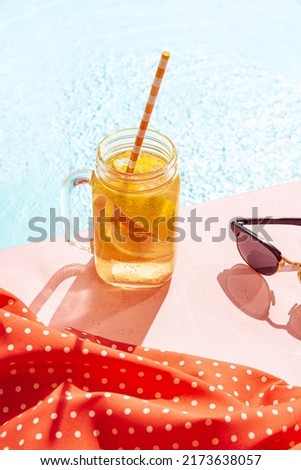 Orange lemonade. Cold drink on a hot summer day. Cocktail glass near swimming pool over blue sky background. Vacation, happiness, summer vibes and ad concept. Vintage retro style