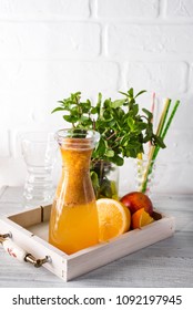 Orange lemonade in the decanter on a wooden tray with ftuits and mint