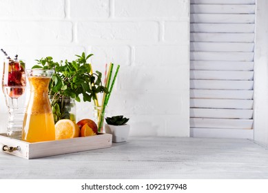 Orange lemonade in the decanter on a wooden tray with ftuits and mint