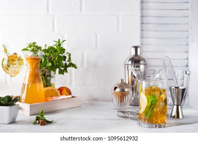 Orange lemonade in the decanter on a wooden tray, cocktail glass with ice, mint and ginger and Cocktail shaker with a place for your subject and text