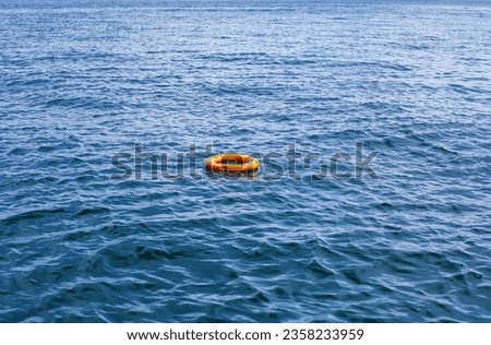 Orange life buoy floating in vast expanse of sea. Red lifebuoy float on ocean waves. Lifeguard equipment with rope swimming in lake. Concept of help, rescue, drowning, saving, surviving, protect, safe