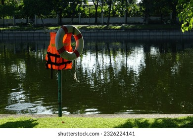 Orange life jacket and white float Hang it by the pond in the park. To be used in an emergency if someone falls into the water.