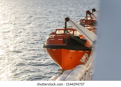 Orange Lifeboat On Side Of North Sea Ferry Boat Crossing Channel To France Or Holland For Passengers To Escape Sinking Ship. Emergency Life Preserve With Number 12 On The Side In Black Font.