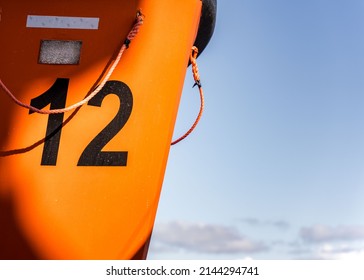 Orange Lifeboat On Side Of North Sea Ferry Boat Crossing Channel To France Or Holland For Passengers To Escape Sinking Ship. Emergency Life Preserve With Number 12 On The Side In Black Font.