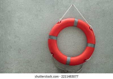 Orange Lifebuoy With Grey Strips (Rescue Ring Buoy) 
Hanging On Small Gravel Wall Near Swimming Pool, Has Space On Left Side For Creative. Life Preserver, Selective Focus.