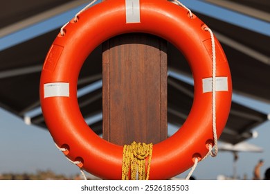 Orange lifebuoy with a rope hanging on wooden pier fence on the sea coast, maritime security life buoy - Powered by Shutterstock