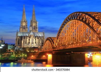 Orange Light On The Hohenzollern Bridge Across Rhine River And Gothic Cathedral In Cologne, Germany