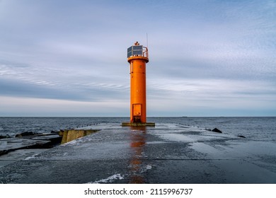 An orange lighthouse at the end of the Mangalsala or Eastern pier in Riga, Latvia where the river Daugava flows into the Baltic Sea. Winter storm, cold weather, ice and snow.