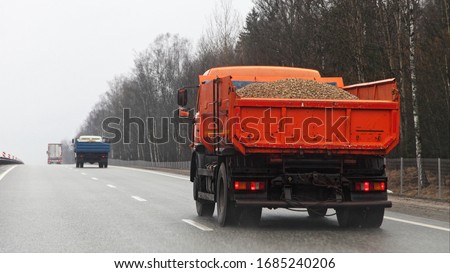 Orange loaded dump truck with gravel drive on highway road at spring day