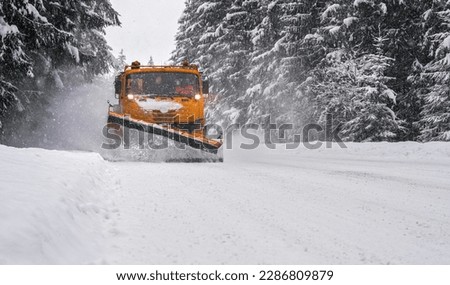 Orange maintenance plough truck on forest road after snowstorm blizzard. Roads get dangerous during winter (driver face blurred unrecognizable)