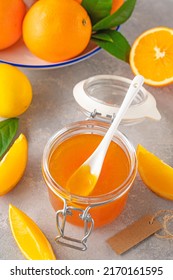Orange marmalade or orange jam in a pot with fresh fruits on a gray background. Copy space.