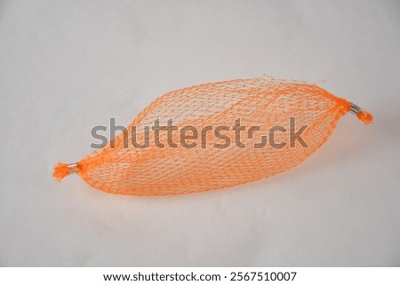 An orange mesh bag, empty and isolated on a light background.