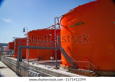 Orange metal storage tanks with acid and its formula on sulfuric (sulphuric) acid plant warehouse. Clear blue sky