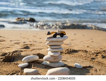 Orange Mini Toy Backhoe Loader Stands On Tower Of Flat Stones Against Backdrop Of The Sea. Vacation In A Construction Company. The Concept Of Stability And Prosperity In The Construction Business