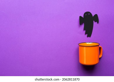 Orange Mug On A Purple Background With Terrible Halloween Decorations. The Concept Of The Halloween Holiday. Drink, Fun, Party. Copy Space, Mock Up, Flatly