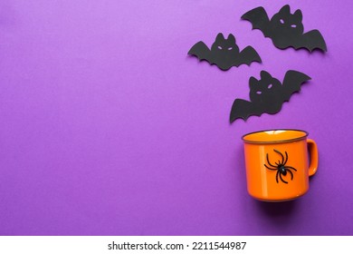 Orange Mug On A Purple Background With Terrible Halloween Decorations. The Concept Of The Halloween Holiday. Drink, Fun, Party. Copy Space, Mock Up, Flatly