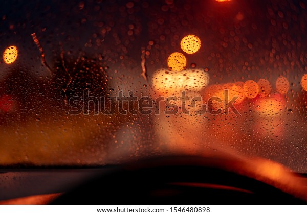 Orange night light bokeh from street light on\
traffic jam day. Rainy day. Transparent glass window with rain\
drop. Romantic weather. City life. Blur abstract background of\
urban light on rainy\
season