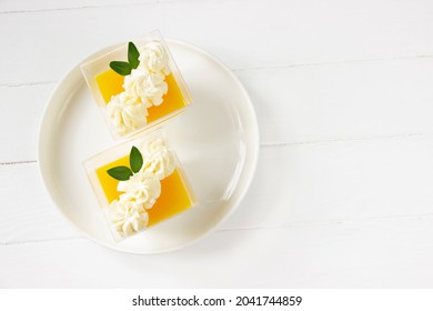 Orange Panna cotta  , delicious italian dessert with whiped cream, portion dessert in a clear plastic cups. White wooden board, healthy eating , healthy dessert, italian dessert background