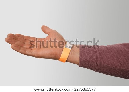 orange paper wristband mockup on persons arm. Clear adhesive bangle wristlet sticker with entry number on hand of middle-aged european man, blue paper bracelet, check tape, event ticket concept