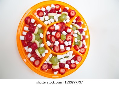 An Orange Party Platter Filled With  Healthy Colorful Fruit (Strawberries, Grapes, Bananas), Marshmallows, And Grinch Fruit Kabobs 