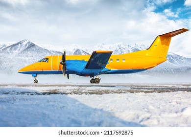Orange passenger turboprop aircraft on the winter airport apron on the background of high scenic mountains