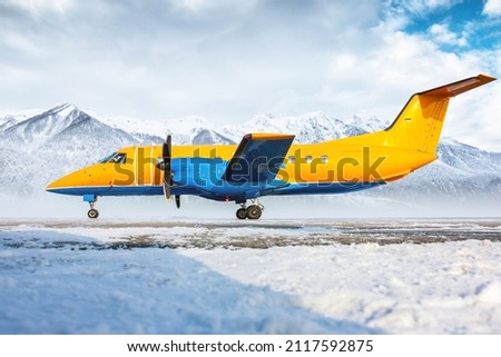 Orange passenger turboprop aircraft on the winter airport apron on the background of high scenic mountains
