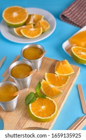 Orange And Peppermint Ice Cream With Pieces Of Orange On Wooden Cutting Board With Light Blue Background