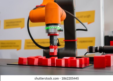 Orange Pick And Place Robotic Clamp Arm Manipulator Moving Red Toy Blocks At Modern Robot Trade Show, Exhibition. Manufacturing, Engineering, Industrial, Ai, Automated Technology Concept