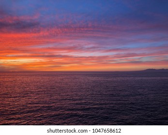 Orange, pink, red, purple, colorful clouds in sunset over water ocean with island in background