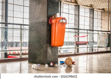 Orange Plastic Garbage Can With Overflow Junk And Litter On The Ground Polluting Indoor Space Of The Building