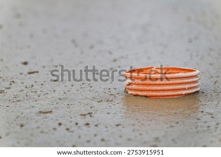 An orange plastic pipe partially embedded in wet concrete with scattered dirt and debris on the surface, representing construction and building materials.