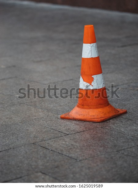 Orange plastic safety cone with strips of retro\
reflective film on the sidewalk paved with granite tiles in Moscow,\
Russia.