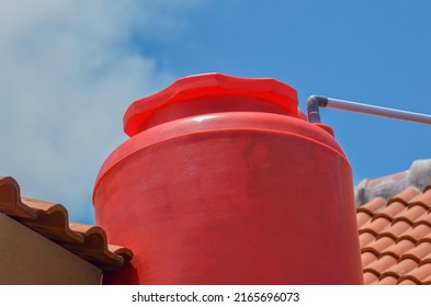 An Orange Plastic Water Storage Tank On A Tiled Roof Of A House Against A Clear Sky Background