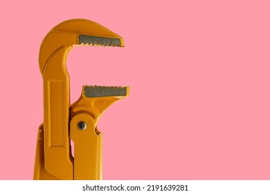 orange plumber wrench on a pink background. pipe wrench