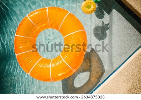 Orange pool float and pineapple cup in a sunlit swimming pool