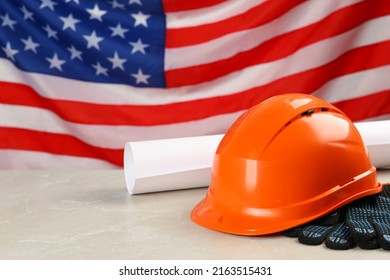 Orange Protective Hard Hat, Gloves, Construction Drawing On Light Grey Table Against American Flag. Space For Text