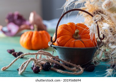 Orange Pumpkin In A Copper Bucket And Dried Berries With Rope And Dry White Herbs On A Blue Wooden Surface. Shallow Depth Of Field. Copy Space.