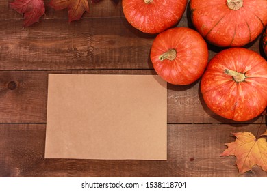 Orange pumpkins, dry fall maple leaves, blank paper for text message on dark brown wooden table. Welcome Autumn, harvest festival, Halloween, Thanksgiving concept. Top view, copy space