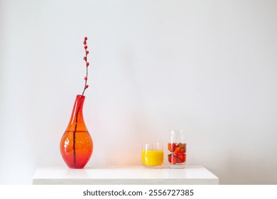 Orange red glass vase and dried flowers orange juice and strawberries soaked in water are placed on a white table - Powered by Shutterstock