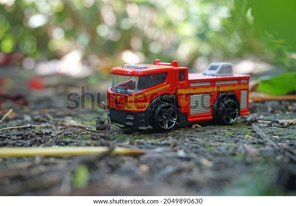Orange and red little toy truck - fire emergency car in\
leaves on the ground. Photo on the background of branches.        \
