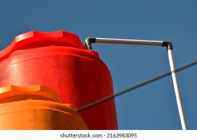 Orange And Red Plastic Water Storage Tank Tank With Stretch Of White Pipe On Blue Sky Background