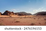 Orange red sand desert, rocky formations and mountains background, blue sky above - typical scenery in Wadi Rum, Jordan