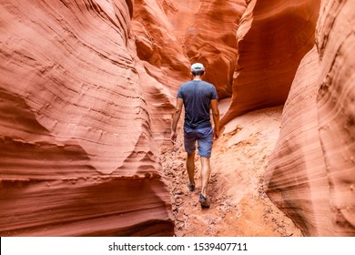 Orange red wave shape formations rocks shadows with back of man walking at narrow Antelope slot canyon in Arizona on footpath trail from Lake Powell