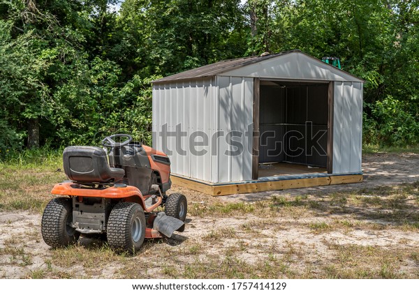 Orange riding\
mower outside a metal tool\
shed.