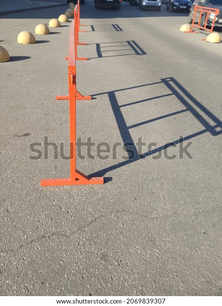 An orange road block stands on the asphalt and casts
a shadow on the road