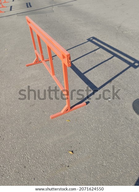 An orange road block stands on the asphalt and casts\
a shadow on the road