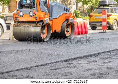 Orange road vibratory roller compacting fresh asphalt on a summer day. City street background. Copy space.